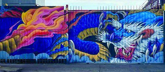 Mural of a blue dragon with white whiskers decorates a fence.