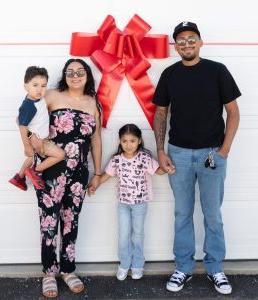 A happy family stands in front of their new home with a red bow affixed to the garage door. 